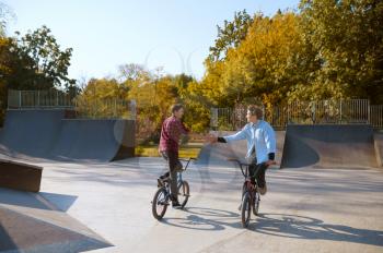 Two bmx bikers, training on ramp in skatepark. Extreme bicycle sport, dangerous cycle exercise, street riding, biking in summer park
