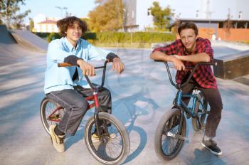 Bmx riders on bikes, training on ramp in skatepark. Extreme bicycle sport, dangerous cycle exercise, street riding, teens biking in summer park