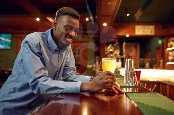 Young man drinks fresh beer at the counter in bar. People relax in pub, night lifestyle, male person with glass of alcohol beverage