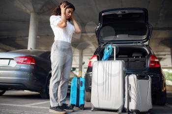 Young woman with suitcases in a panic, car parking. Female traveler with luggage in vehicle park lot, passenger with many bags. Girl with baggage near automobile