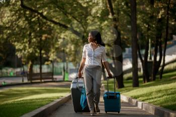 Woman with two suitcases on walkway in summer park. Female traveler with luggage leisures outdoors, passenger with bag resting in nature. Girl with baggage relax on city alley