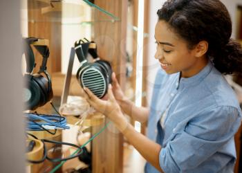 Woman holds vintage headphones in audio components store. Female person in music shop, showcase with earphones on background, buyer in multimedia salon
