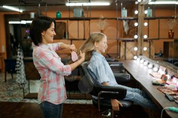 Mother and daughter do their hair in salon. Mom and little girl play hairdressers together, happy childhood, glamour family