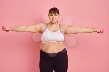 Overweight woman doing exercise with dumbbells, pink background, body positive. Obesity fighting, striving for a healthy lifestyle