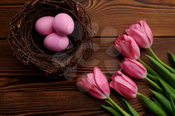 Pink tulips and easter eggs in decorative nest on wooden background. Spring flowers blooming and paschal food, fresh floral decoration, holiday celebration symbol