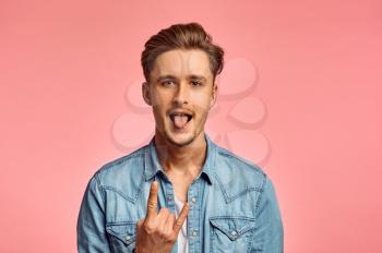 Young man shows his tongue, pink background, emotion. Face expression, male person looking on camera in studio, emotional concept, feelings