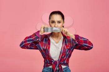 Young woman taped her mouth shut, pink background, emotion. Face expression, female person looking on camera in studio, emotional concept, feelings