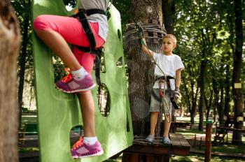 Little girl and boy in equipment climbs in rope park. Child climbing on suspension bridge, extreme sport adventure on vacations, danger entertainment outdoors