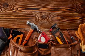 Hammer, stapler and screwdrivers, measuring tape and hacksaw in leather case on wooden background, nobody. Professional instrument, carpenter equipment, fastening, tapping and screwing tools