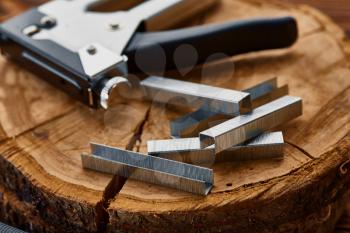 Metal stapler and steel staples on stump, macro view, wooden background, nobody. Professional instrument, carpenter equipment, woodworker tools
