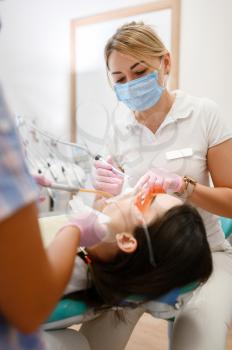 Female dentist works with patient tooth in clinic, stomatology. Doctor in uniform, medical worker, medicine and health, professional teeth care, dentistry