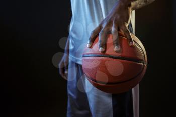 Strong basketball player hand holds ball in studio, black background. Professional male baller in sportswear playing sport game, tall sportsman