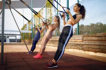 Sportive women doing fit exercise with ropes on sports ground, outdoors group training. Female athletes in sportswear, team fitness workout, teamwork