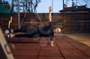Sportive man doing balance exercise with ropes on sports ground outdoors. Slim female person in sportswear, outside fitness training, fit workout