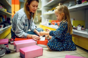 Mother and little baby opens box with shoes in kid's store. Mom and adorable girl near the showcase in children's shop, happy childhood, family makes a purchase in market