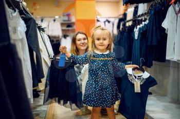 Mother and little baby choosing skirt in kid's store. Mom and adorable girl near the showcase in children's shop, happy childhood, family makes a purchase in kid's market