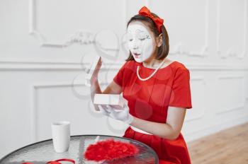Female mime artist in red costume, scene with gift. Pantomime theater, parody comedian, positive emotion, humour performance, funny face mimic and grimace