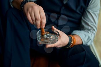 Man puts out a cigar in an ashtray, closeup view. Tobacco smoking culture, specific flavor. Male smoker leisures in office