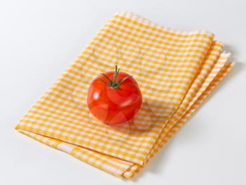 Fresh red tomato on checked yellow tea towel