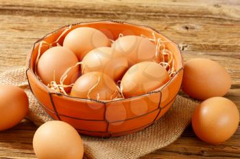 Fresh brown eggs in terracotta bowl and next to it on wooden table