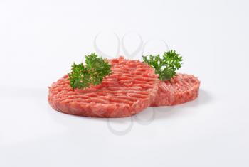 two raw hamburger patties with parsley on white background