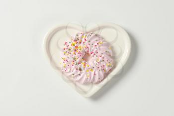 Pink meringue wreath cookie topped with sprinkles on heart shaped plate