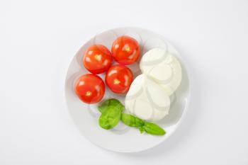 fresh mozzarella, basil and tomatoes - ingredients for caprese salad on white plate