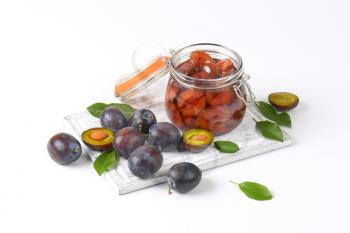 Plum compote in an open glass jar and fresh plums next to it on cutting board