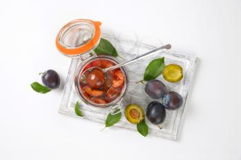 Plum compote in an open glass jar and fresh plums next to it on cutting board