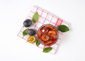 Damson compote in a glass bowl and fresh plums next to it on checked dishcloth