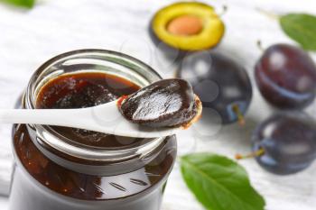 thick plum jam on plastic spoon and in a jar