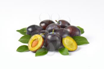 pile of ripe plums with leaves on white background