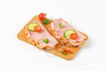 two open faced ham sandwiches on wooden cutting board