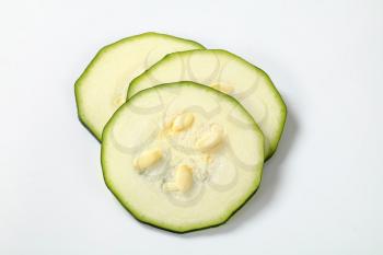 three thin slices of fresh zucchini on a white background