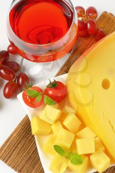 yellow medium-hard cheese with eyes, glass of red wine and fresh grapes