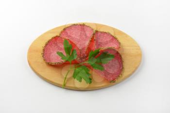 slices of green pepper coated salami on wooden cutting board