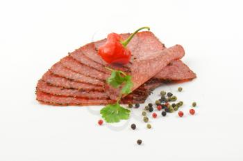 Thin slices of black pepper salami with peppercorns and red chili pepper