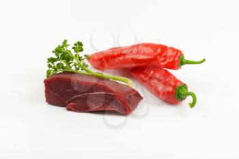 raw beef rump, fresh parsley and red peppers on white background