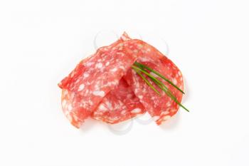 slices of dry salami and chives arranged on white background
