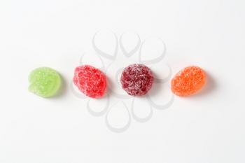 four fruit jelly candies coated with sugar on white background