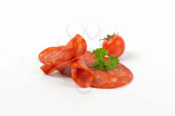 slices of chorizo salami with parsley and cherry tomato on white background