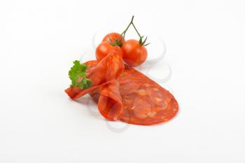 slices of chorizo salami with parsley and cherry tomatoes on white background