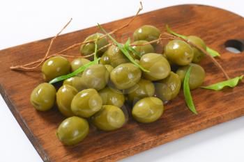 heap of green olives on wooden cutting board - close up