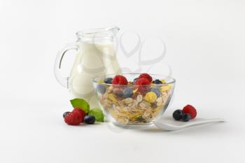 bowl of mixed breakfast cereals with fresh raspberries and blueberries, and jug of milk