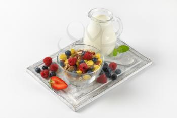 bowl of mixed breakfast cereals and jug of milk on wooden cutting board