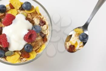 spoon and bowl of mixed breakfast cereals with fresh raspberries and blueberries and yogurt