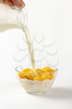 milk pouring into bowl of corn flakes on white background