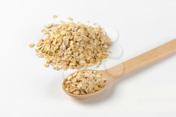 pile of oat flakes and wooden spoon on white background