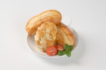 whole and sliced mini baguettes on white plate