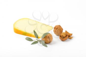 slice of gouda cheese with walnuts and sprig of sage on white background